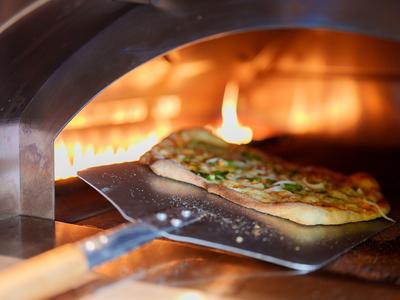 Ein frischer Fladenbrotpizza wird aus einem Steinofen mit Flamme geschoben.