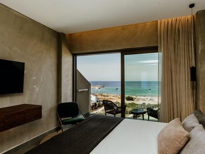 Modernes Hotelzimmer mit Meerblick, großem Bett und Glasfenstern mit Zugang zum Balkon.