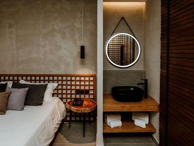 Modernes Hotelzimmer mit weißem Bett, hölzernem Nachttisch und rundem Spiegel an Wand.