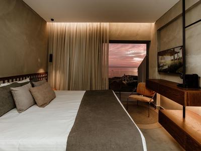 Modernes Hotelzimmer mit großem Bett, Sitzbereich und Blick auf den Sonnenuntergang.