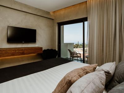 Modern eingerichtetes Hotelzimmer mit Balkon, Fernseher und gemütlichem Bett mit Kissen.