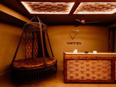 Gemütlicher Spa-Empfang mit Korbsessel und beleuchtetem Deckenpaneel in warmen Tönen.