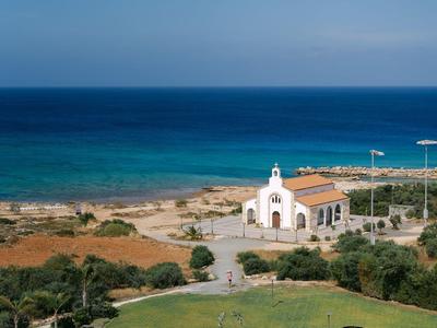 Blick auf eine Kirche am Meer mit grünem Rasen und klarem blauem Himmel.