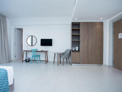 Helles Hotelzimmer mit weißem Boden, Schreibtisch, Stühlen und Schrank mit Holzfronten.