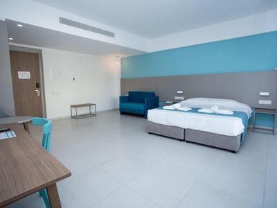 Modernes Hotelzimmer mit Doppelbett, Sitzbereich und Schreibtisch in hellen Farben.