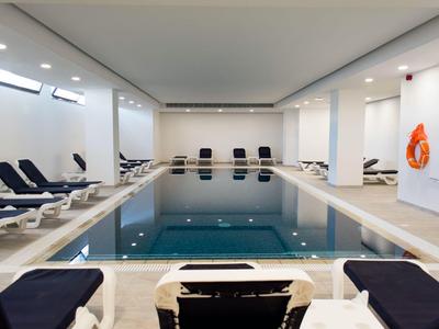 Ein heller Innenpool mit blauen Liegestühlen und hellen Wänden in einem Hotel.