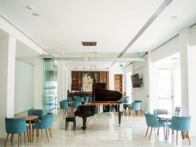 Heller Hotel-Loungebereich mit Flügel und türkisen Sesseln an Tischen auf hellem Boden.