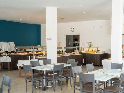 Moderner Frühstücksraum mit Tischen, Stühlen und einem Buffetbereich in einem Hotel.