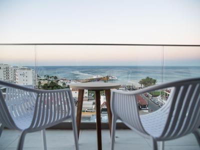 Balkon mit zwei Stühlen und Tisch mit Meerblick und höher gelegenen Gebäuden im Hintergrund.