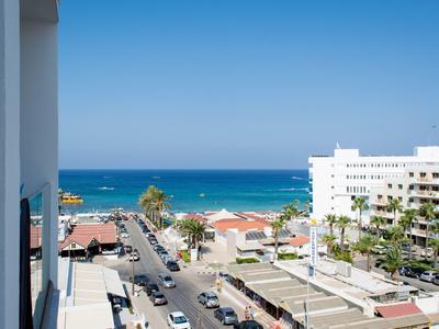 Blick auf eine Küstenstraße mit Blick auf das blaue Meer und weiße Gebäude unter klarem Himmel.