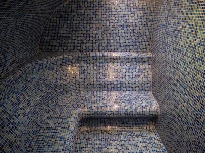 Innenaufnahme einer Dampfbadkabine mit blauen Mosaikfliesen bedeckten Wänden und Sitzgelegenheiten.