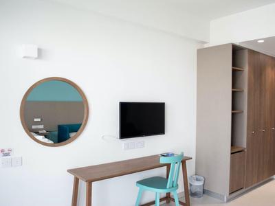 Modern eingerichtetes Hotelzimmer mit einem Schreibtisch, Stuhl, TV und rundem Spiegel an der Wand.