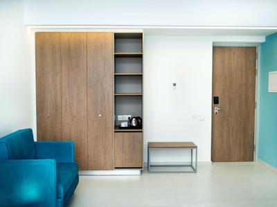Moderner Hotelzimmerbereich mit blauem Sofa, Holzschrank und kleiner Sitzbank an weißer Wand.