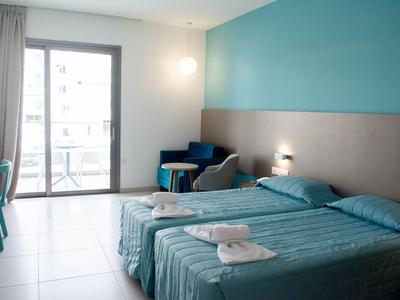 Helles Hotelzimmer mit zwei Einzelbetten, Balkon und modern eingerichteter Sitzecke.