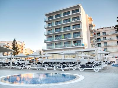 Modernes Hotel mit Pool und zahlreichen Liegestühlen bei klarem Himmel.