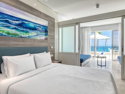 Camera d'hotel moderna con letto bianco e vista mare attraverso grandi finestre.