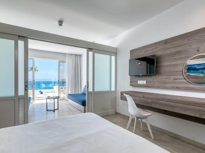 Camera d'hotel moderna con vista mare, scrivania e TV, arredamento luminoso e minimalista.