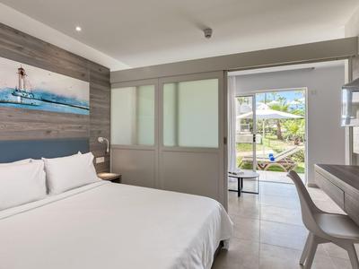 Camera d'hotel moderna con letto matrimoniale, scrivania e accesso a una terrazza con vista piscina.