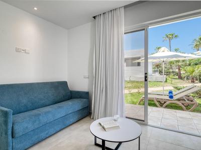 Area camera d'hotel moderna con divano blu, tavolo rotondo bianco e vista sulla terrazza con lettino.