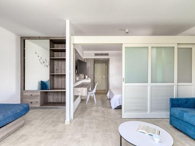 Camera d'albergo luminosa con divani blu, tavolino e porta aperta verso la camera da letto.