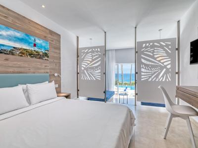 Camera d'hotel moderna con letto grande, balcone e vista sulla piscina e sul mare.