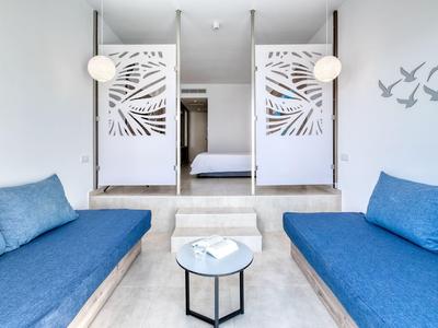 Camera d'hotel moderna con due divani blu e tende bianche a motivo davanti a un letto