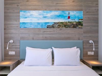 Letto moderno con cuscini bianchi e testiera blu contro parete in legno con foto di paesaggio.