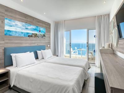 Camera d'hotel moderna con due letti, vista mare attraverso grandi finestre, arredamento luminoso.