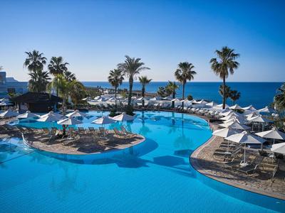 Grande piscina con lettini e palme vicino al mare sotto un cielo sereno.