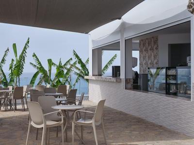 Area esterna moderna con tavoli, sedie e piante accanto a un bar dell'hotel.