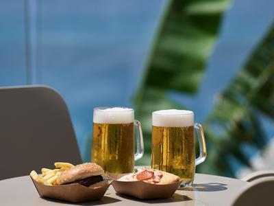 Due boccali di birra e piccoli snack su un tavolo con uno sfondo sfocato di foglie di palma.