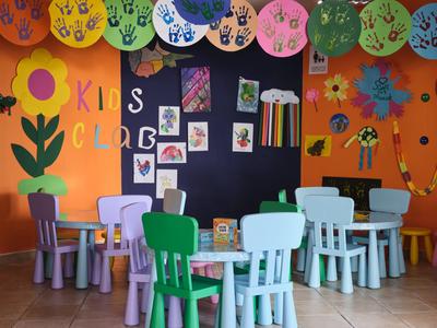 Camera per bambini colorata con piccoli tavoli, sedie e decorazioni murali di carta.