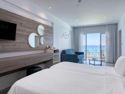 Modernes Hotelzimmer mit Doppelbett, Sesseln und Balkon mit Meerblick.