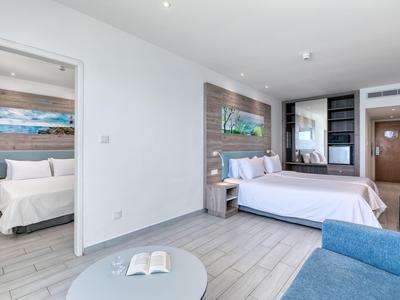 Modernes Hotelzimmer mit zwei Betten, hellen Wänden und einem blauen Sofa.