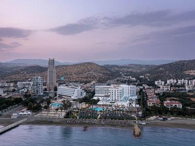 Stadt mit hohen Gebäuden, Hügeln im Hintergrund und Strand mit Promenade im Vordergrund bei Abendlicht.