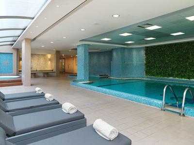 Moderner Hallenbadbereich mit blauen Liegen, Pool und grünem Wandpflanzen-Dekor.