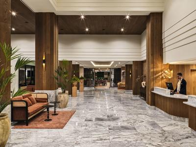 Große Hotellobby mit Marmorfußboden, Holzwänden, Sitzgruppen und Empfangstresen.
