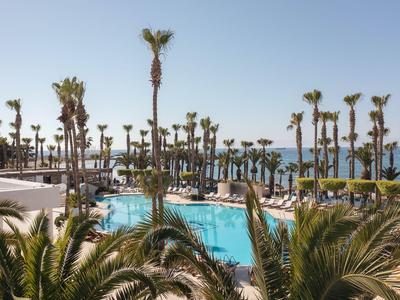 Área de piscina con palmeras y tumbonas bajo un cielo azul claro junto al mar
