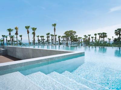 Piscina exterior moderna con escalones claros de agua y palmeras al fondo bajo un cielo azul.