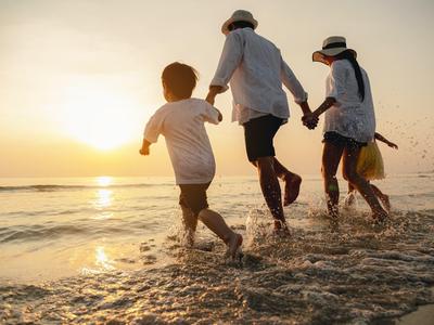 Familie rennt am Strand ins Wasser bei Sonnenuntergang, Silhouetten vor hellem Himmel.