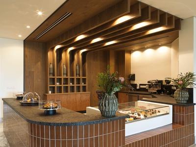 Área de bar moderna en hotel con paneles de madera, mostrador central y plantas.