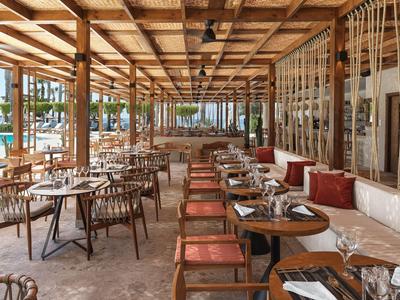 Área de restaurante abierta con techo de madera, mesas y sillas, decorada con cojines y vajilla.