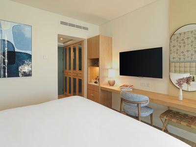 Modernes Schlafzimmer mit weißem Bett, Holzschreibtisch, rundem Spiegel und blauem Stuhl.