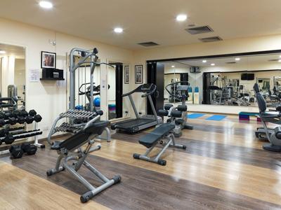 Gimnasio brillante de hotel con cintas de correr, pesas y máquinas en suelo de madera.