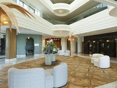 Große, helle Lobby mit Holzboden, Sitzgruppen, Pflanzen und moderner Deckenarchitektur.