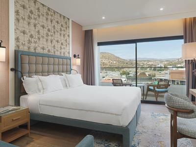 Modernes Schlafzimmer mit großem Bett, Nachttischen, Stühlen und bodentiefen Fenstern mit Bergblick.