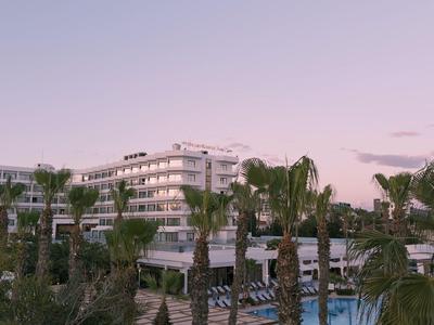 Hotel moderno con palmeras y piscina al atardecer.