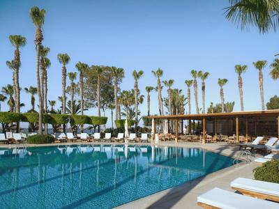 Gran piscina con tumbonas y palmeras en un resort soleado.