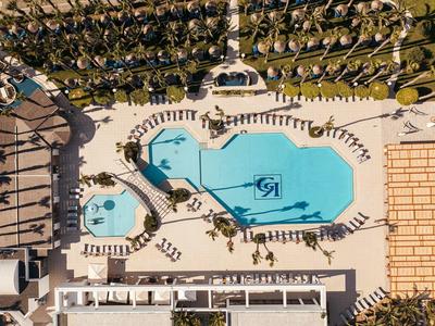 Vogelperspektive auf eine große, geformte blaue Poolanlage mit umliegenden Liegestühlen und Palmen.