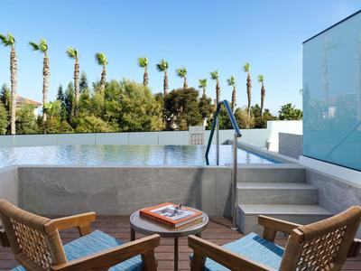 Moderner Balkon mit Pool, zwei Stühlen, kleinem Tisch und Palmen im Hintergrund bei klarem Himmel.
